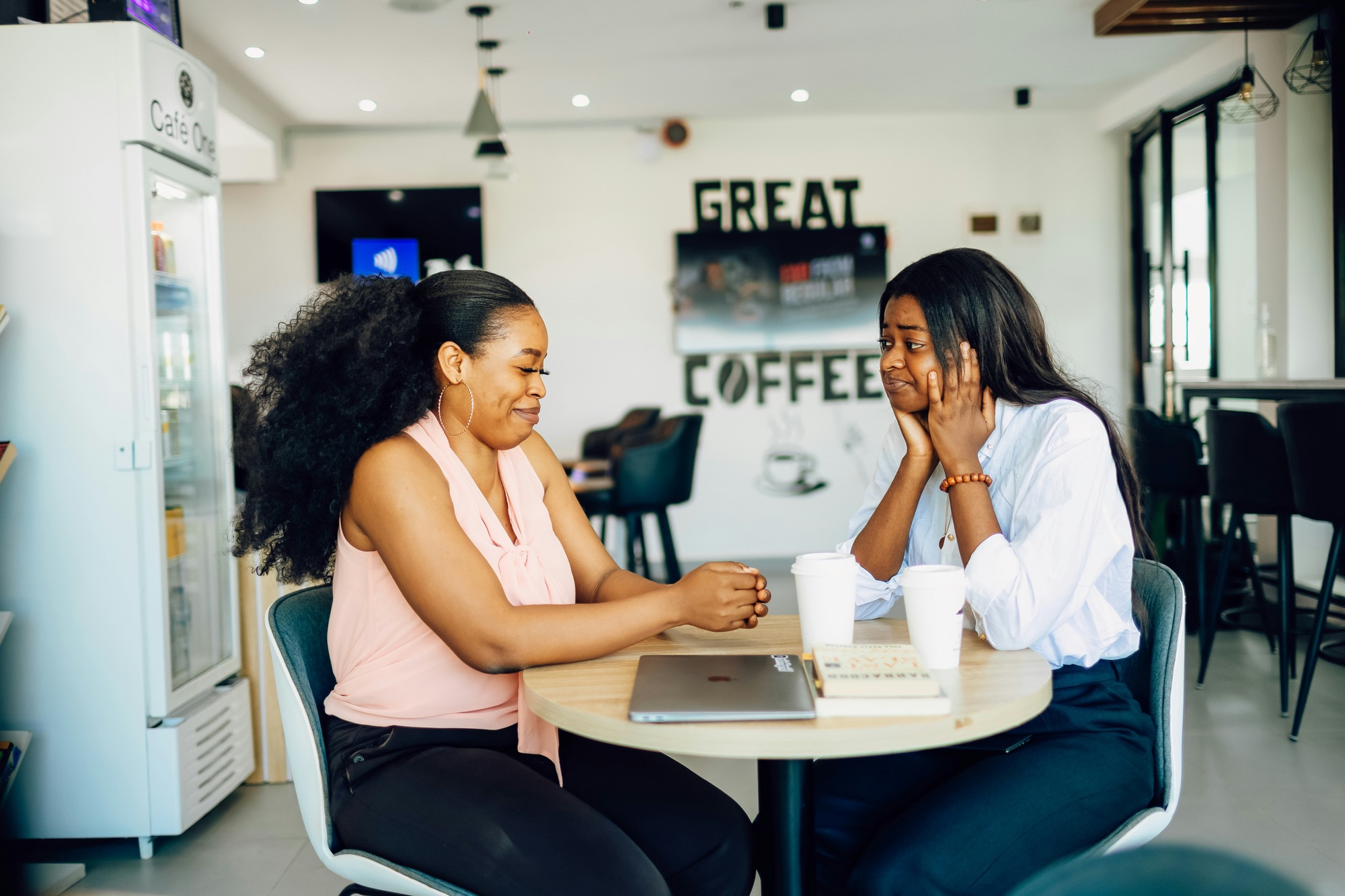 Two Black women talking over coffee at a cafe table during a pick your brain meeting