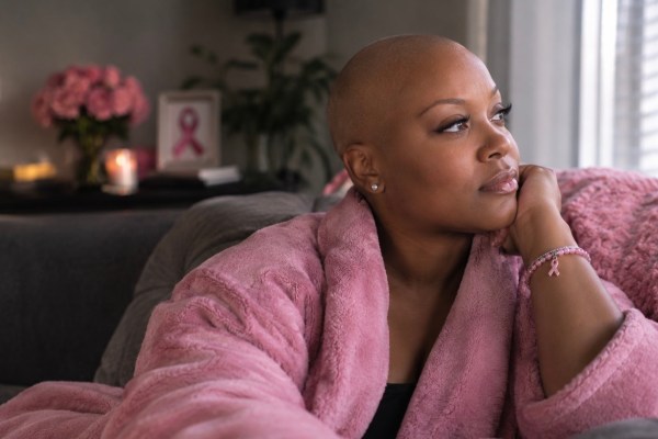 Breast Cancer Awareness Month image of a woman in a pink robe at home with a pink ribbon and roses behind her