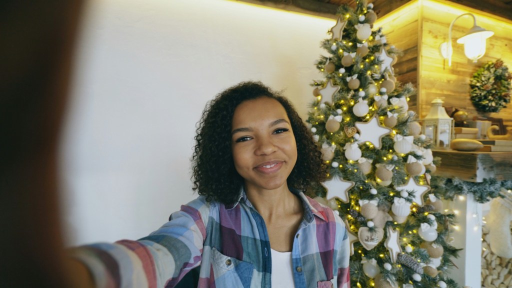 Smiling woman taking a selfie in front of a lit Christmas tree, ready for family holiday questions