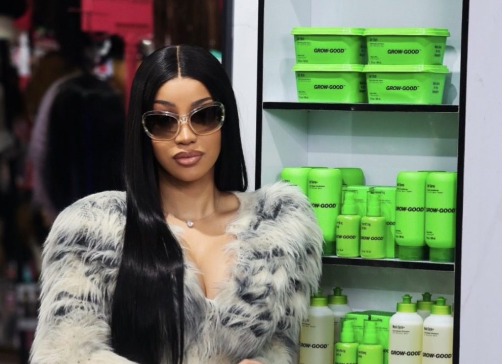 Cardi B poses beside a shelf of Grow-Good Beauty haircare products inside a beauty supply store